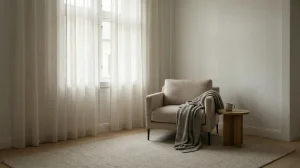 Minimalistyczne wnętrze z jasnym fotelem przy oknie, miękkim światłem i spokojną, uporządkowaną przestrzenią